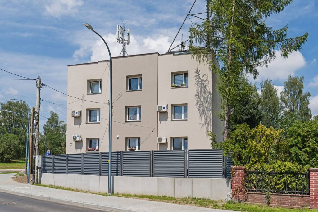 Trzykondygnacyjny budynek wielomieszkaniowy przy ul. Szarych Szeregów w Katowicach po dociepleniu, beżowa elewacja z tynku strukturalnego, widok od ulicy