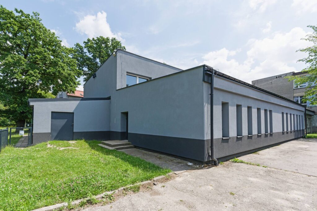 Budynek sali gimnastycznej Szkoły Węgielek przy ul. Karliczka w Katowicach po termomodernizacji: jasnoszara elewacja wykonana metodą lekką mokrą i grafitowy cokół